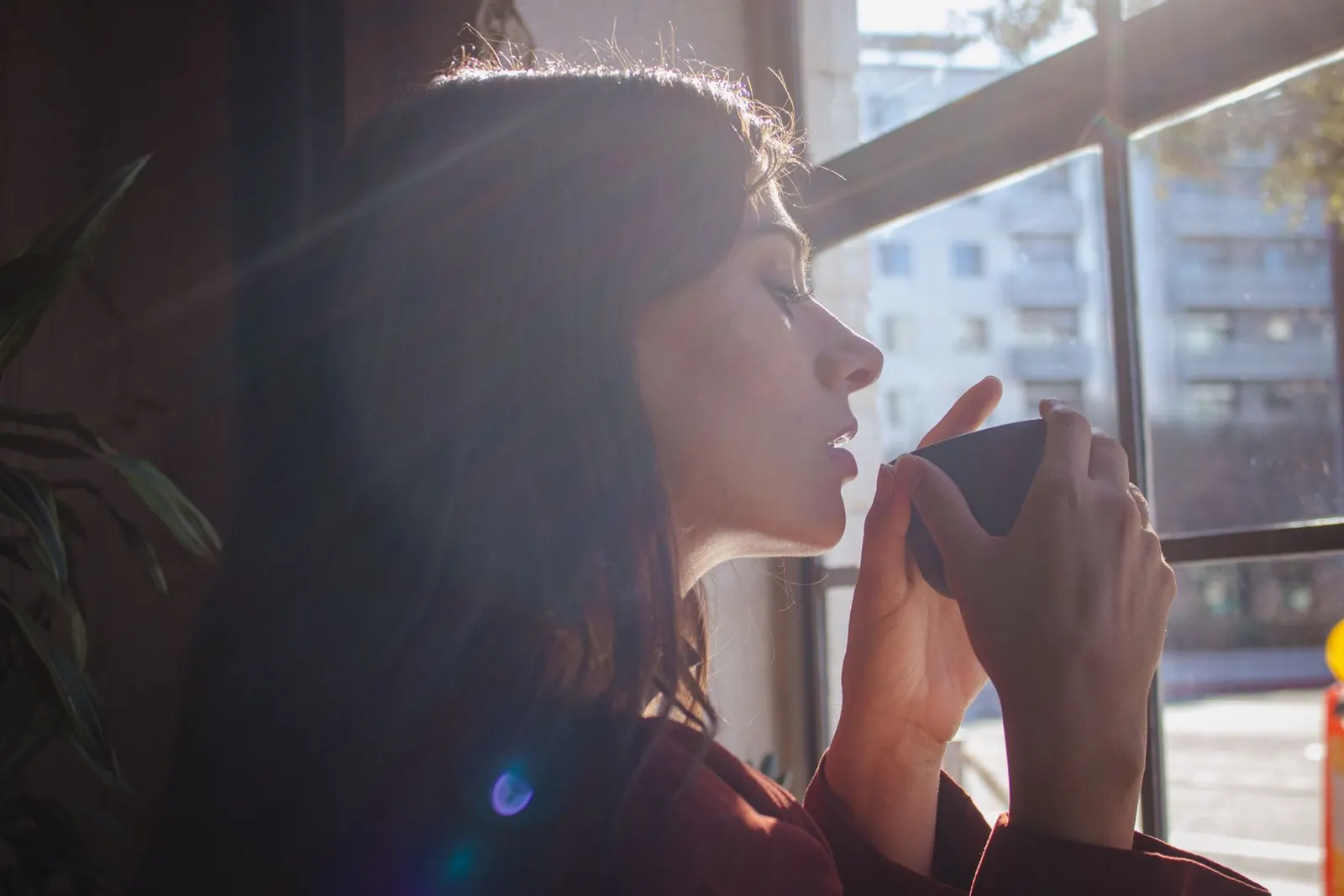 Woman holding a warm drink by a sunlit window