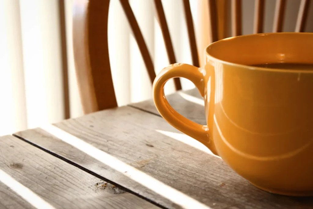 Yellow coffee mug on a wooden table in warm sunlight