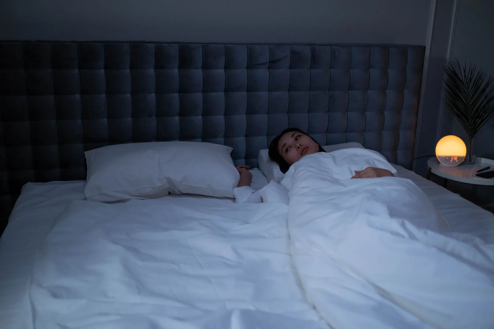 Woman lying awake under white bedding in a dim bedroom