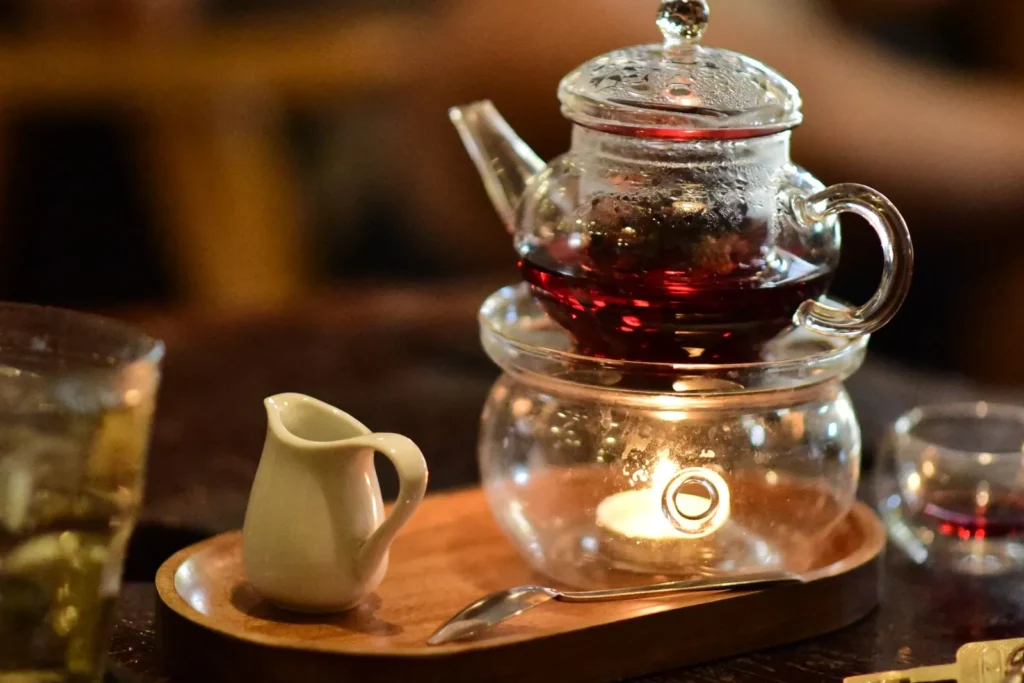 Glass teapot of herbal tea on a wooden tray by candlelight