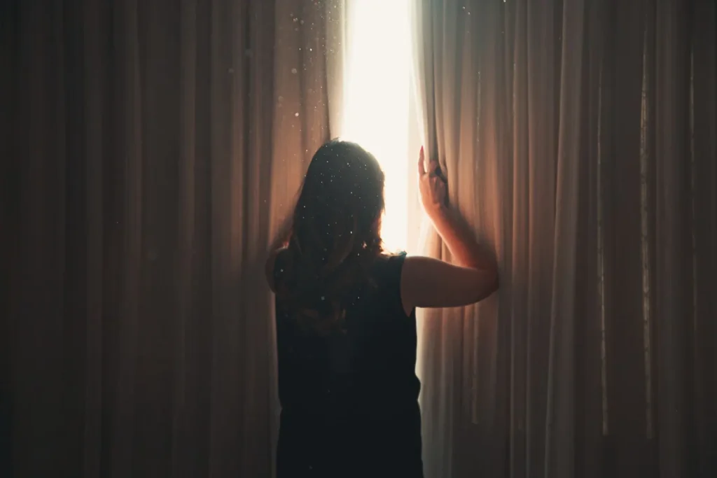 Woman opening a curtain to let morning light into her apartment