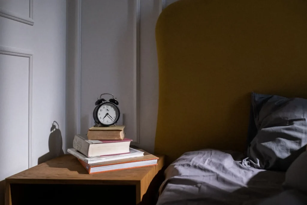 Alarm clock and books on a nightstand beside a bed