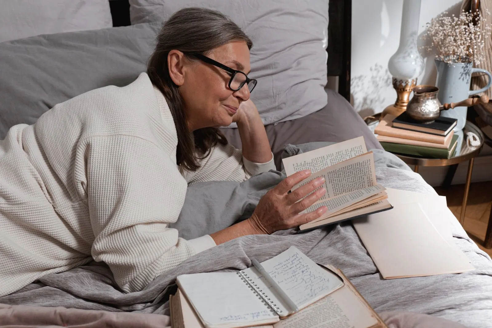 Older woman reading in bed with glasses and a cozy blanket